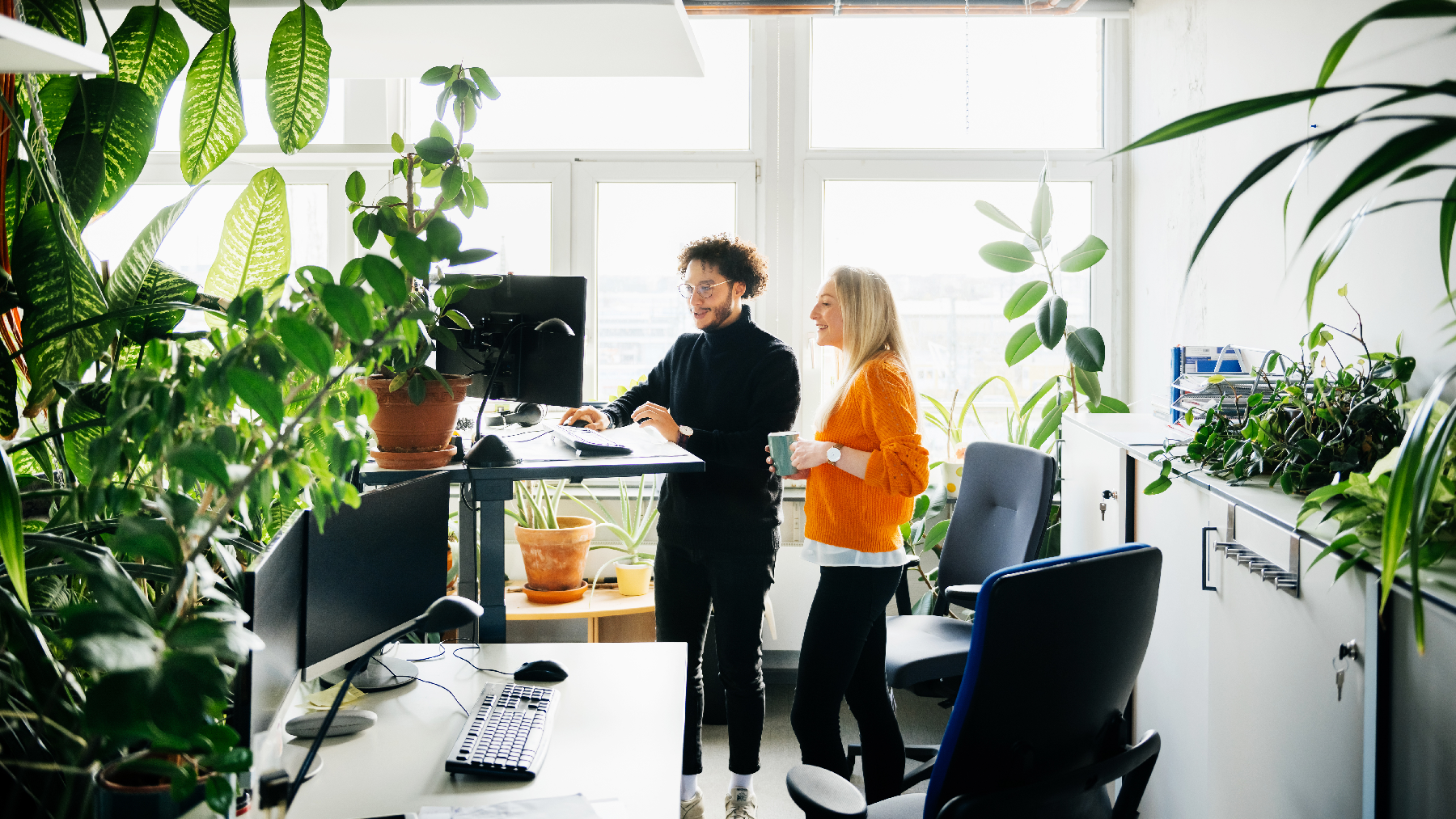 Colleagues working at a standing desk with much greenery throughout the office.